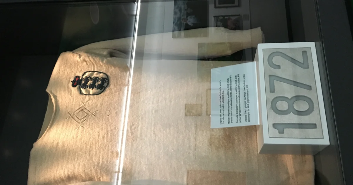 Kostum putih lengan panjang bersulam lambang tiga singa dengan label tahun 1872 di etalase museum