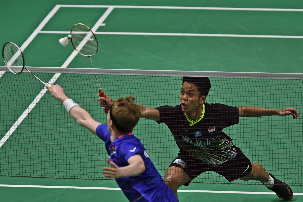 Anthony Sinisuka Ginting berkaus hitam menjangkau kok di depan net melawan Anders Antonsen berkaus biru