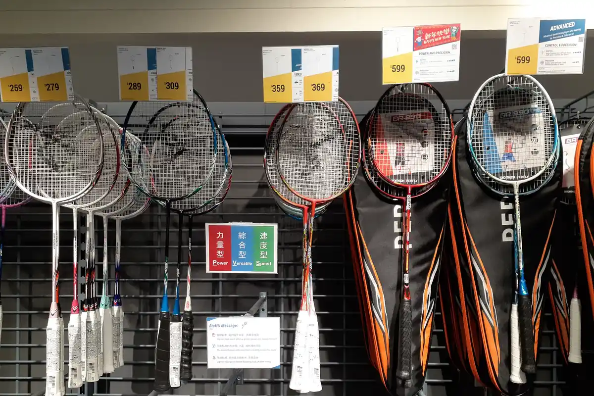 Deretan raket badminton tergantung di rak toko olahraga dengan papan label Power, Versatile, dan Speed