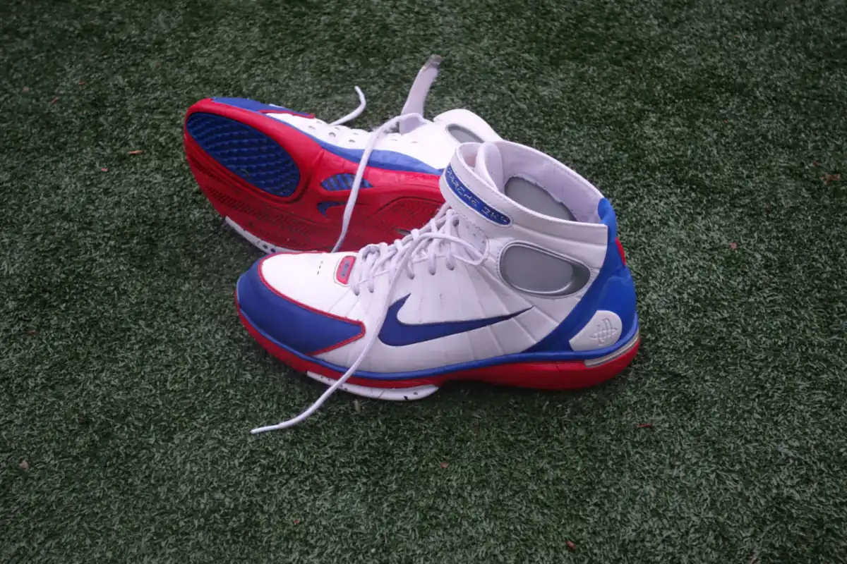 Sepasang sepatu basket Nike Huarache 2K4 putih biru merah di atas rumput sintetis