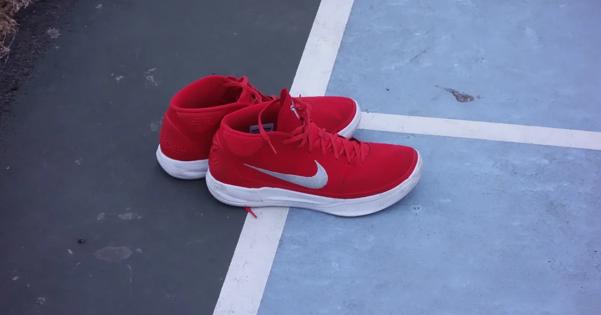 Sepasang sepatu basket Nike Kobe A.D. Mid merah dengan logo swoosh putih di lapangan basket outdoor