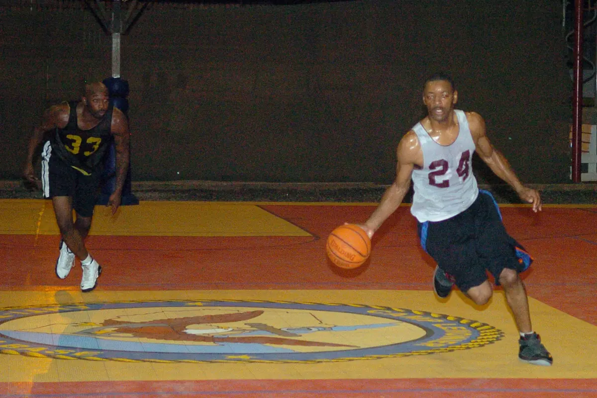 Pemain basket berkaus putih nomor 24 menggiring bola di lapangan indoor beralas kayu kuning