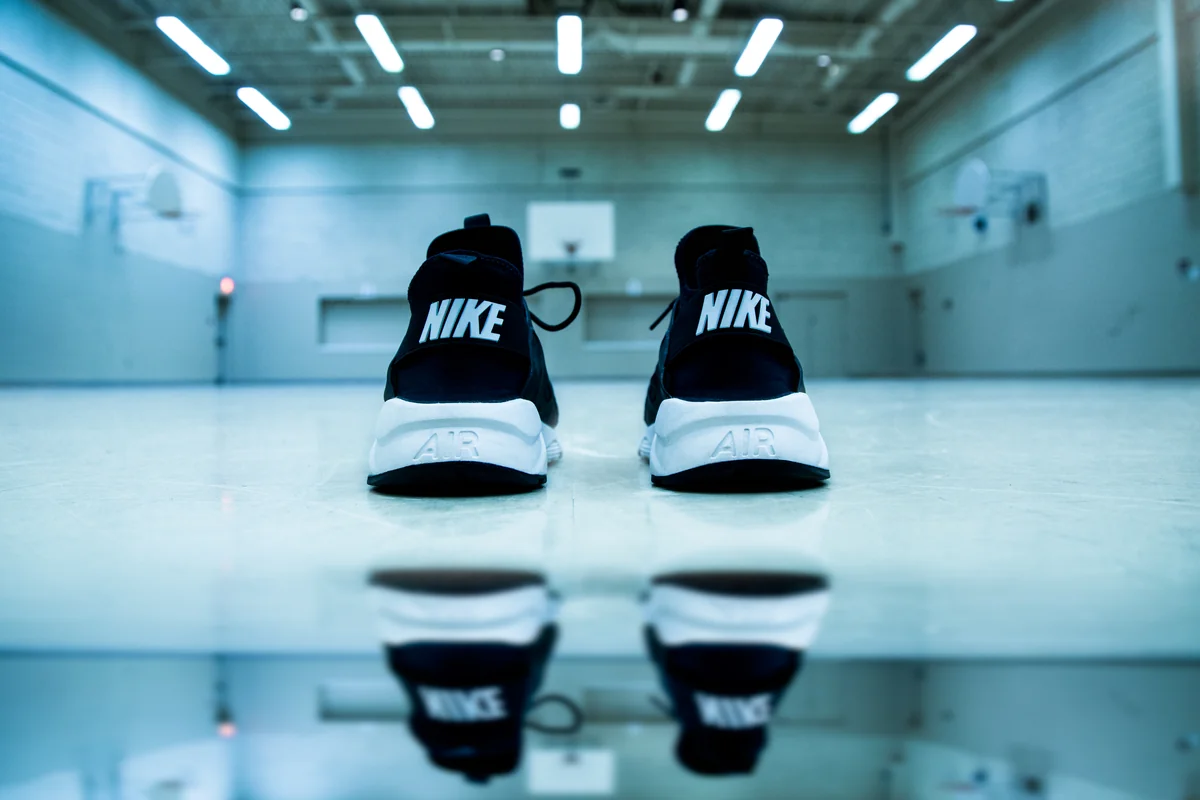 Sepasang sepatu Nike hitam putih berdiri di lantai lapangan basket indoor yang mengilap