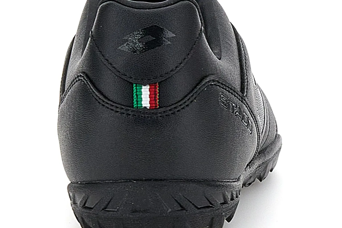 Bagian tumit sepatu Lotto Stadio 700 turf serba hitam dengan logo Lotto timbul dan label kecil bendera Italia