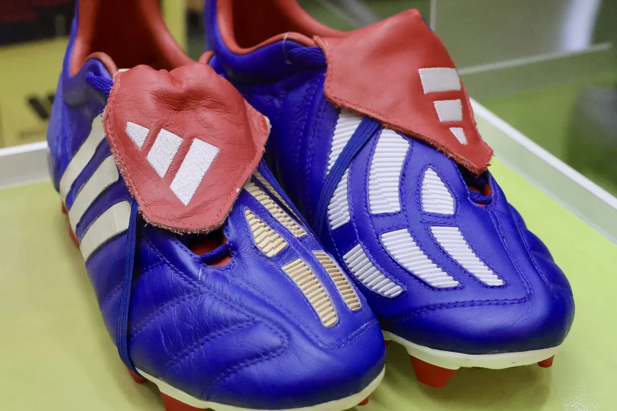 Sepasang sepatu bola Adidas Predator Mania biru dengan lidah merah di dalam etalase