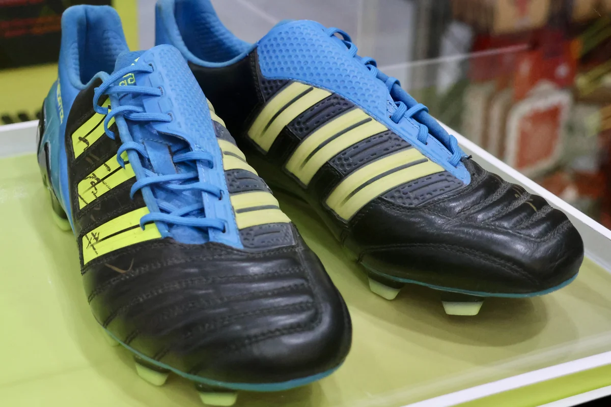 Sepasang sepatu bola Adidas Predator AdiPower hitam biru dengan garis kuning di etalase