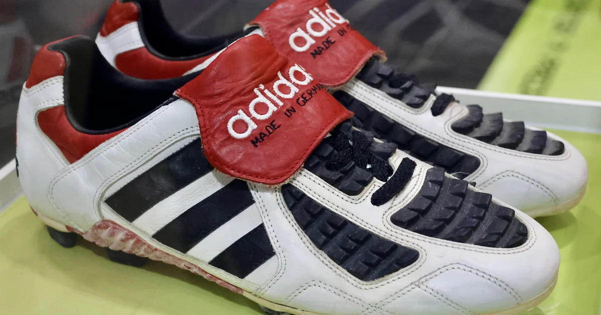 Sepatu bola Adidas Predator Touch putih merah dengan lidah lipat bertuliskan adidas, dipajang di etalase