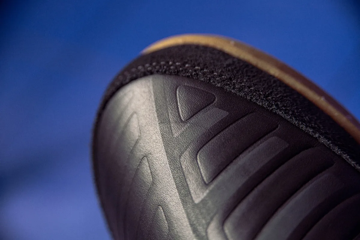 Close-up sol bawah sepatu futsal Umbro berwarna gelap dengan pola alur bersudut dan tepi karet cokelat