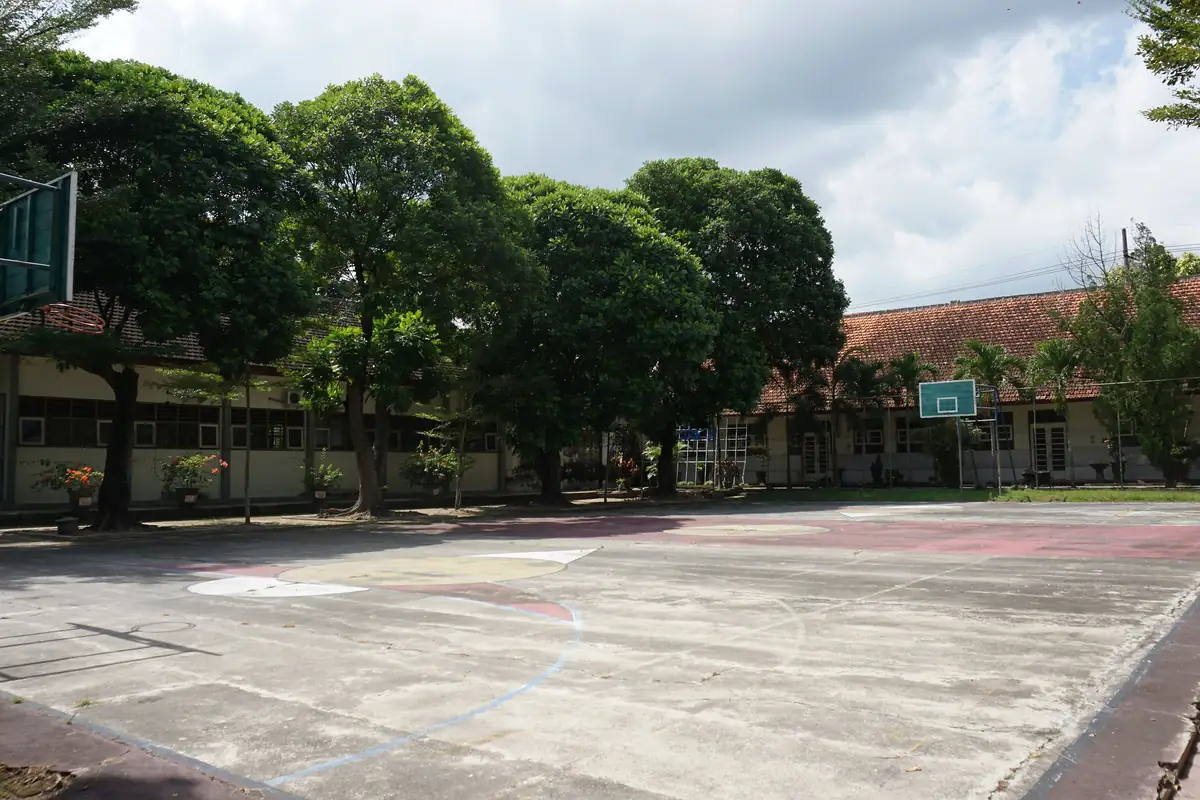 Lapangan futsal terbuka beralas semen di halaman SMAN 1 Blitar dengan pepohonan dan gedung sekolah di latar belakang