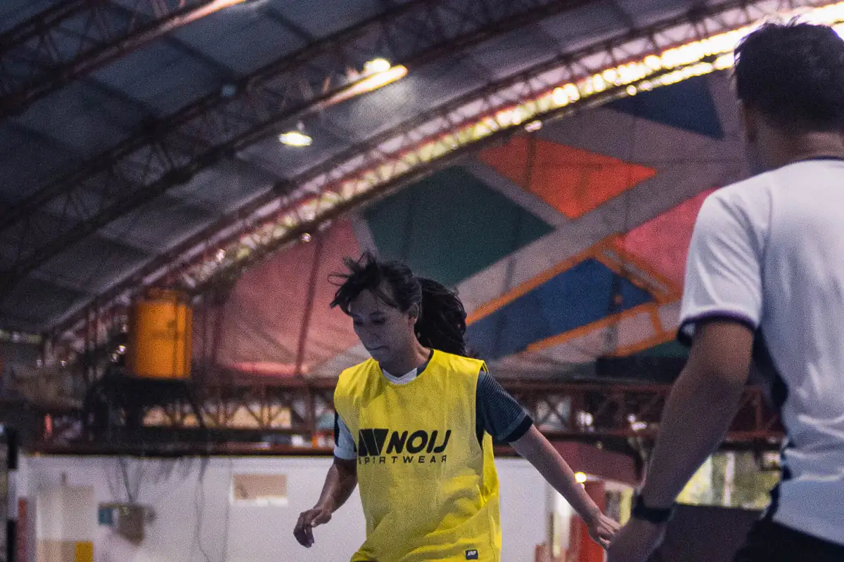 Pemain futsal putri berompi kuning bergerak dibayangi lawan di lapangan futsal interior