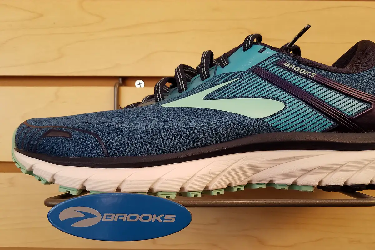 Sepatu lari Brooks Adrenaline GTS 18 biru tua dengan aksen hijau toska di rak pajang kayu