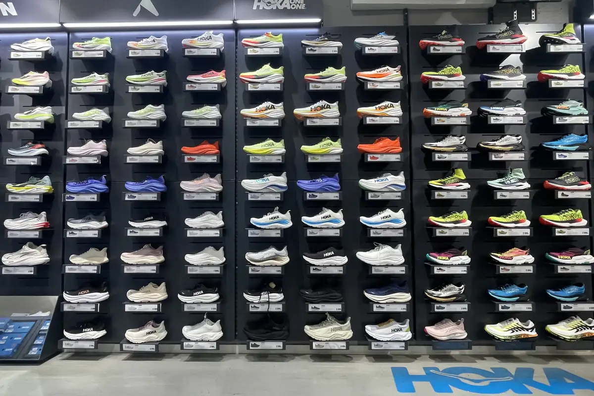 Rak dinding berisi puluhan sepatu lari Hoka berbagai warna di sebuah toko